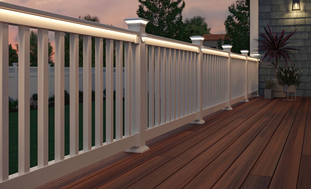 A well-lit white railing lines a wooden deck at sunset. Soft lighting creates a warm ambiance. A potted plant and trees suggest a serene outdoor setting.